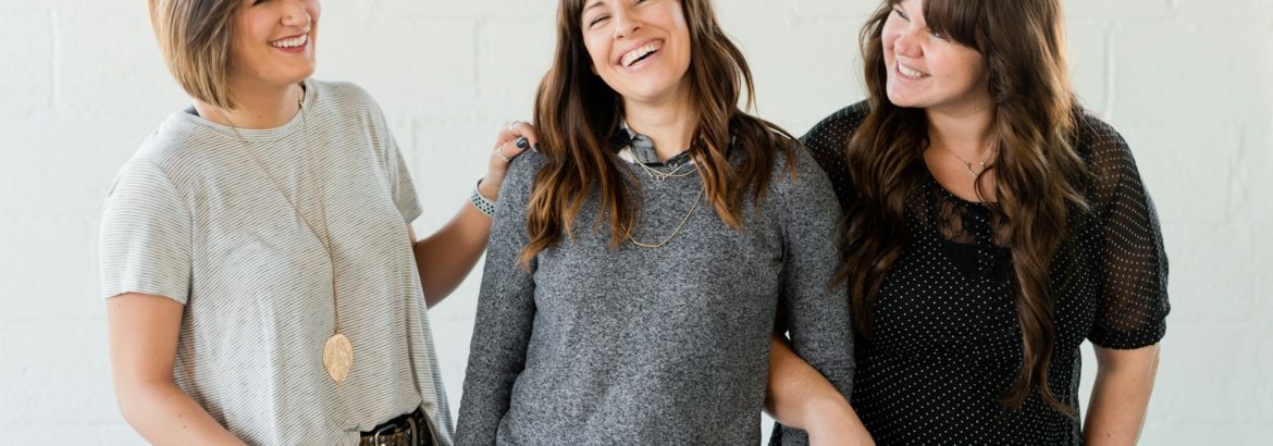 3 women smiling and standing beside white wall